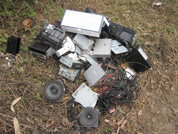 スピーカーやコード、車載機器などが草むらに不法投棄されている写真
