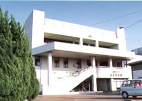 白い外観の2階建てのあおば会館入り口前の駐車場から全体を写した写真