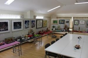沢山の作品(絵画や生け花、ガラスケースに入った人形など)が展示されている室内の写真