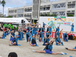 イベントステージ前で水色のハッピを着た子供たちが演技を披露している写真