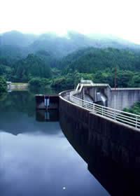 山に囲まれており、水がアーチ型のダムに溜まっている須恵ダムの写真