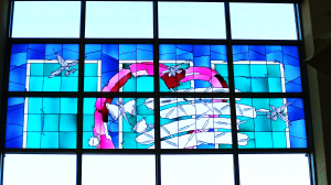 大きな窓に4本の線とハート (シンボル) が描かれたロゴマークがデザインとなっているステンドグラスの写真