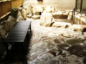 木製のベンチが置かれ、岩や大きな石に囲まれた浴槽のある露天風呂の写真