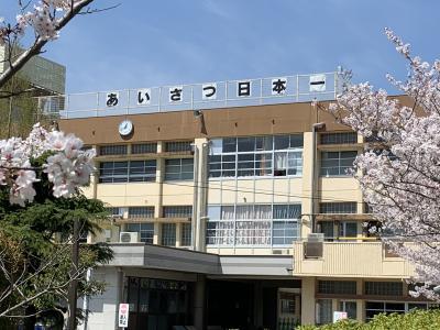 校舎手前に桜が咲いており、校舎の屋上に「あいさつ日本一」と掲げられている写真