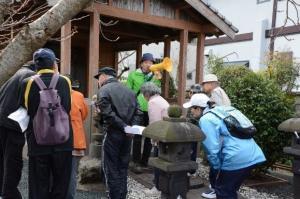 神社に石灯籠があり、黄色の拡声器を持った方が集まっている参加者に話をしている写真